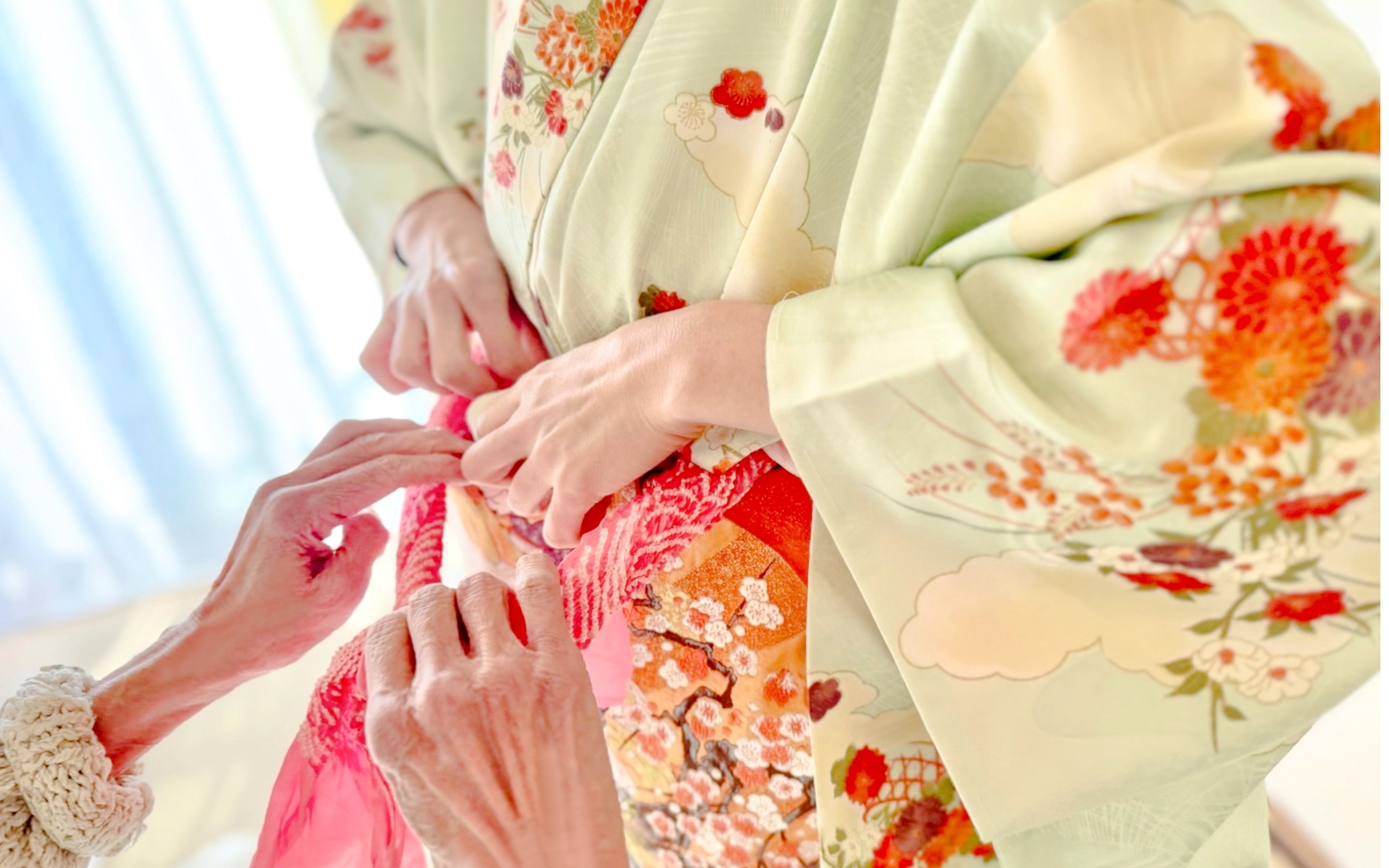 Hands tying an obi on a floral kimono during a rental experience in Tokyo.