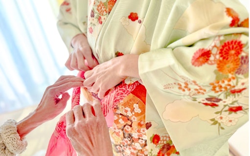 Hands tying an obi on a floral kimono during a rental experience in Tokyo.