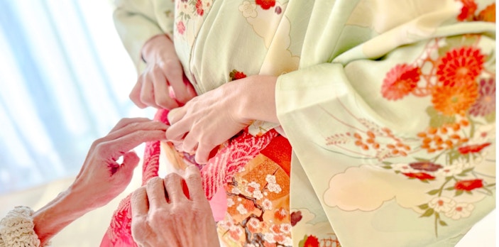 Hands tying an obi on a floral kimono during a rental experience in Tokyo.