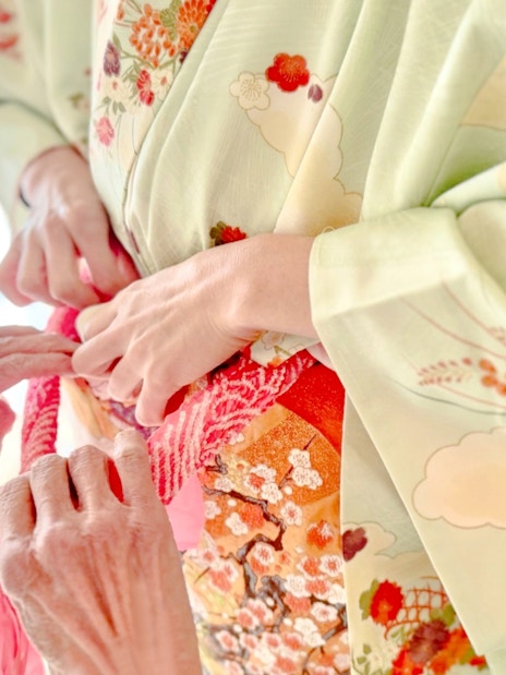 Hands tying an obi on a floral kimono during a rental experience in Tokyo.