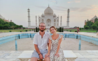 Couple sitting in front of the Taj Mahal at sunrise, Agra tour.