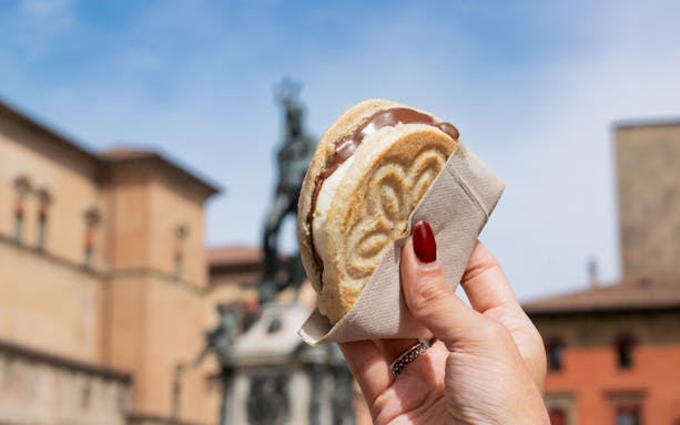 Hand holding an ice cream sandwich in front of a historic building in Bologna.