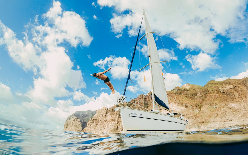 Tourist diving from private boat in Tenerife with cliffs in background.