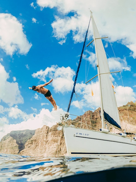 Tourist diving from private boat in Tenerife with cliffs in background.