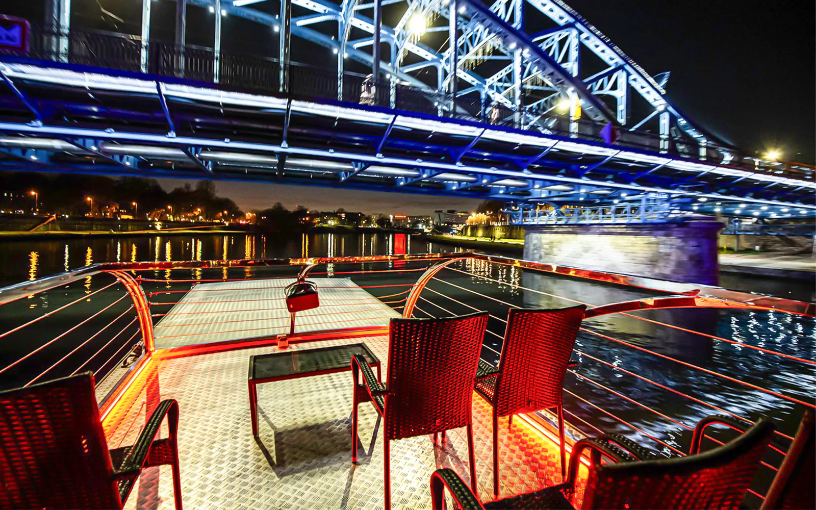 Cruise deck view under illuminated bridge on Vistula River at night in Krakow.