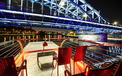 Cruise deck view under illuminated bridge on Vistula River at night in Krakow.
