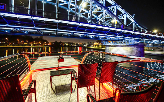 Cruise deck view under illuminated bridge on Vistula River at night in Krakow.