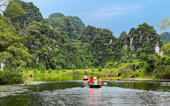Boat tour through lush karst mountains in Trang An Landscape Complex, Ninh Binh, Vietnam.