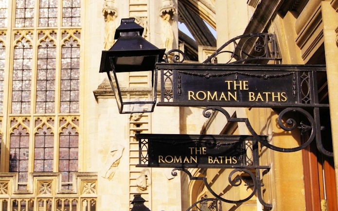 Roman Baths entrance sign in Bath, England, with historic architecture in the background.