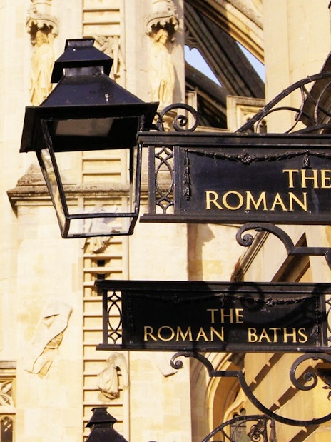 Roman Baths entrance sign in Bath, England, with historic architecture in the background.
