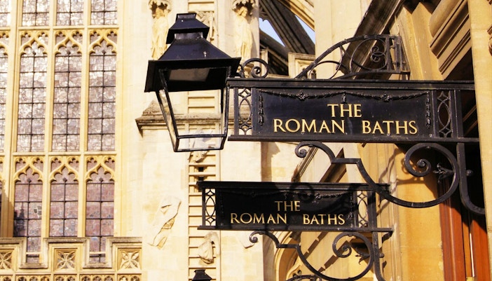 Roman Baths entrance sign in Bath, England, with historic architecture in the background.