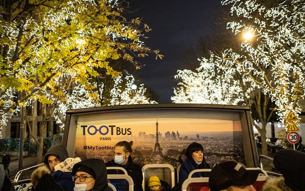 Tootbus night tour in Paris with illuminated trees and passengers on an open-top bus.