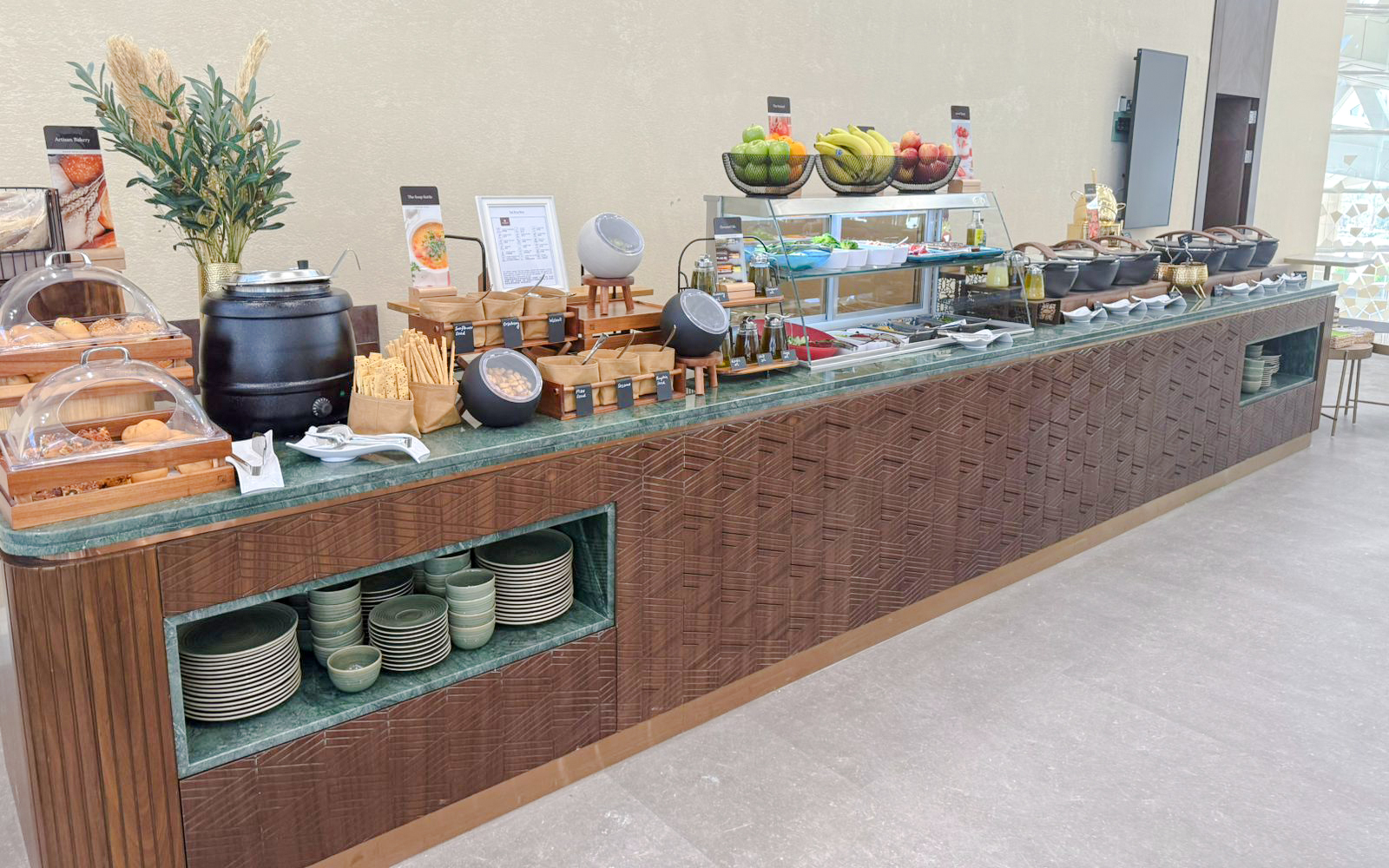 Buffet spread at Plaza Premium Lounge, Riyadh with fruits, pastries, and hot dishes.