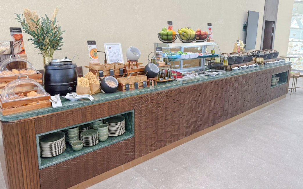 Buffet spread at Plaza Premium Lounge, Riyadh with fruits, pastries, and hot dishes.