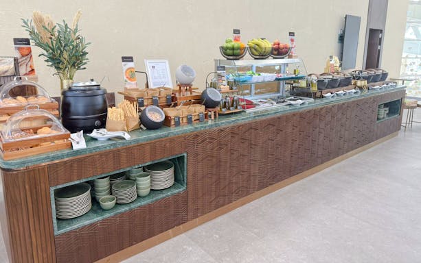 Buffet spread at Plaza Premium Lounge, Riyadh with fruits, pastries, and hot dishes.