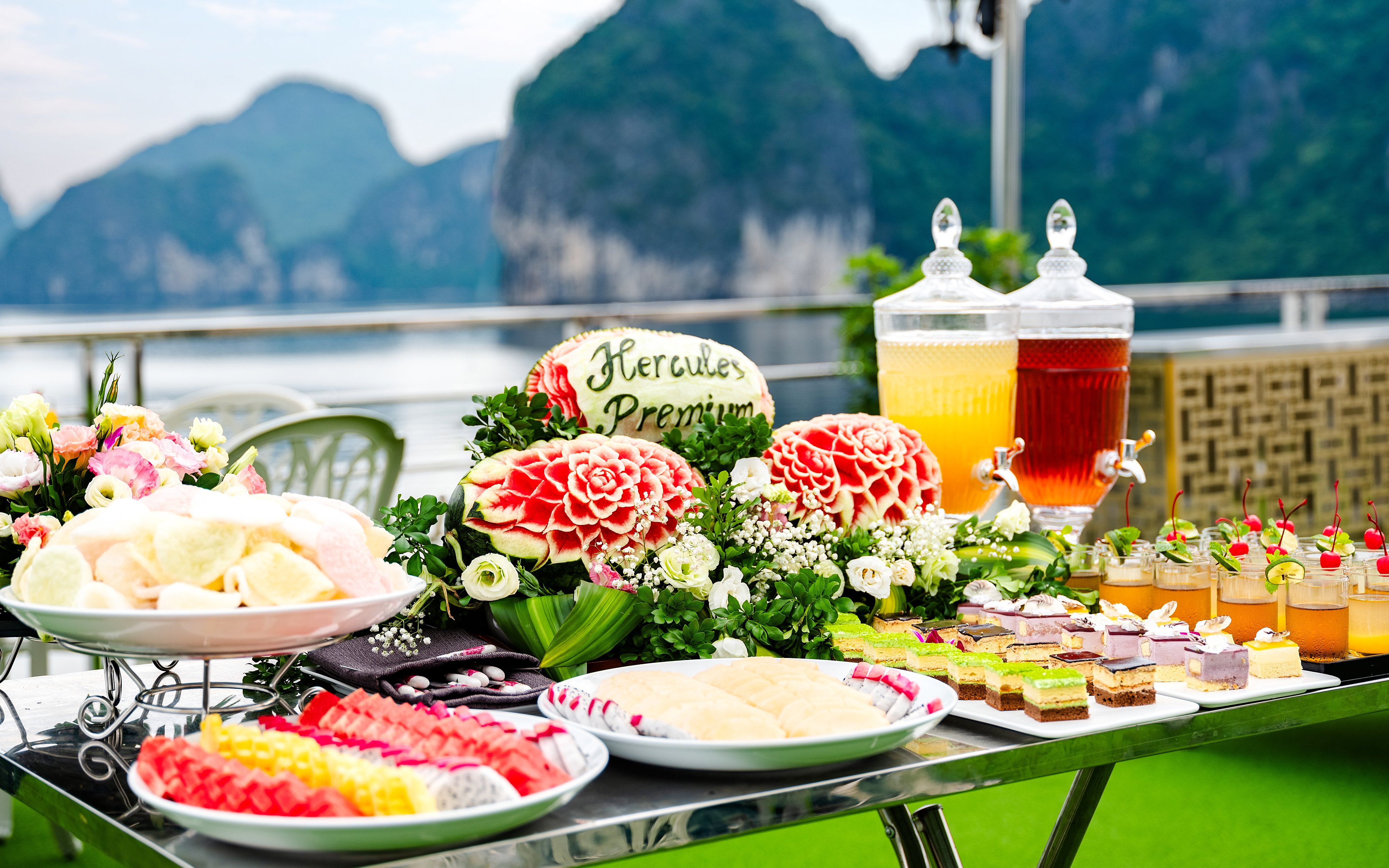 Buffet spread with carved fruit and desserts at Hercules Premium, overlooking scenic mountains.