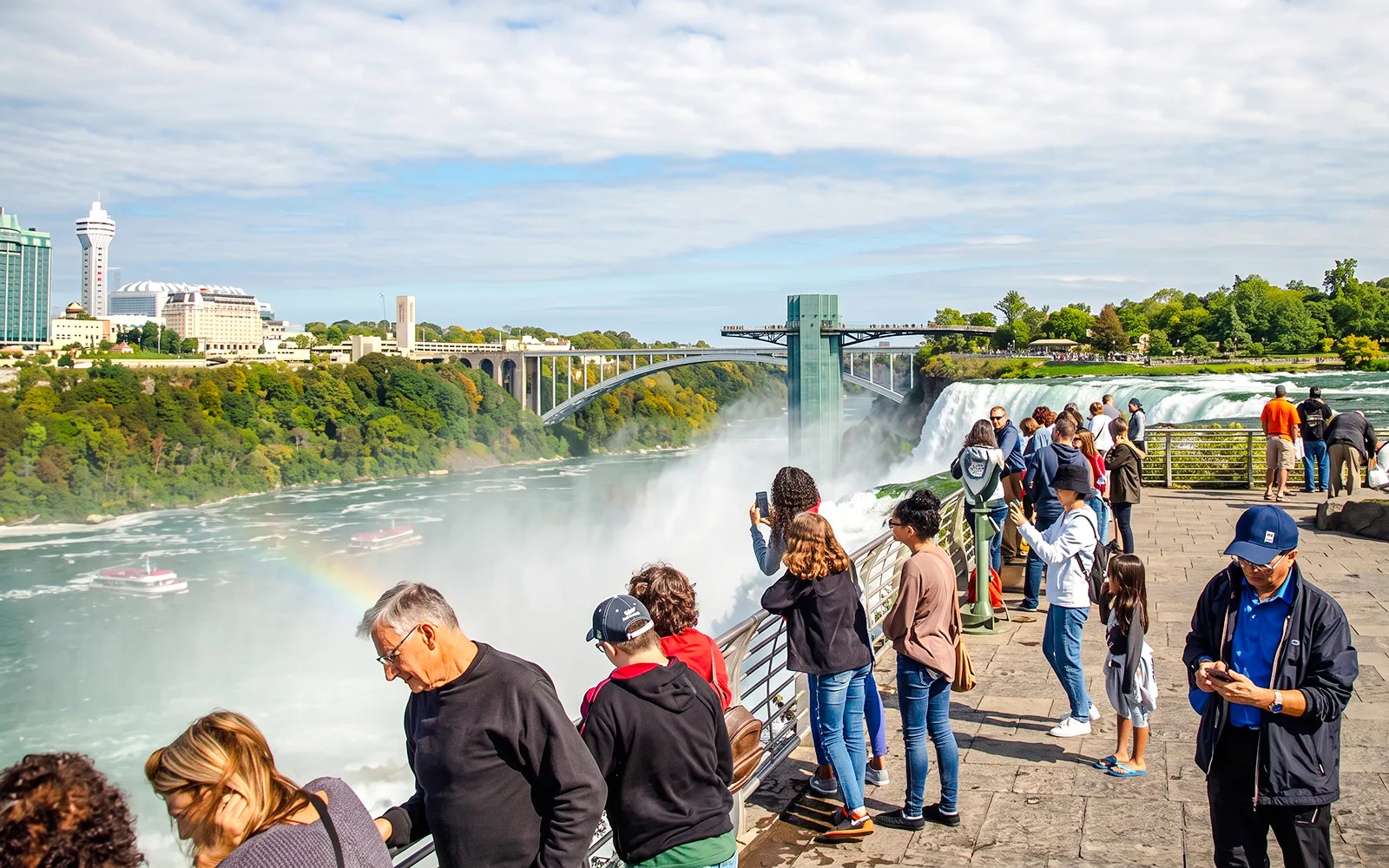 Visitors viewing Niagara Falls with Maid of the Mist boats below and Rainbow Bridge in the background.