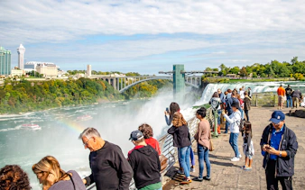 Visitors viewing Niagara Falls with Maid of the Mist boats below and Rainbow Bridge in the background.