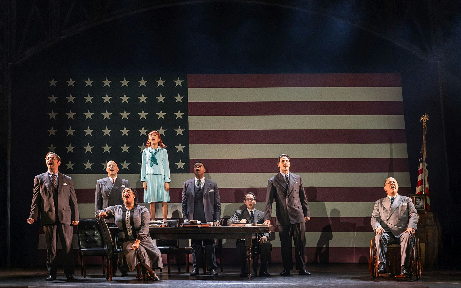 Performers on stage in front of a large American flag during an "Annie" musical scene.