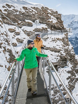 Visitors walking on a snowy cliffside walkway at Grindelwald First, Interlaken.