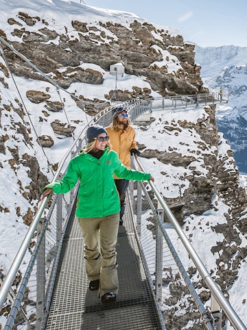 Visitors walking on a snowy cliffside walkway at Grindelwald First, Interlaken.