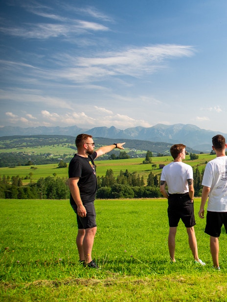 Tourists in a field near Zakopane with a van, enjoying mountain views.
