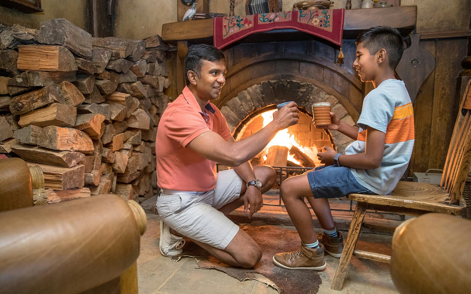 Father and son enjoying drinks by the fireplace at Hobbiton Movie Set, New Zealand.
