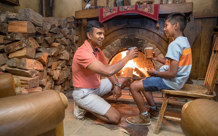 Father and son enjoying drinks by the fireplace at Hobbiton Movie Set, New Zealand.