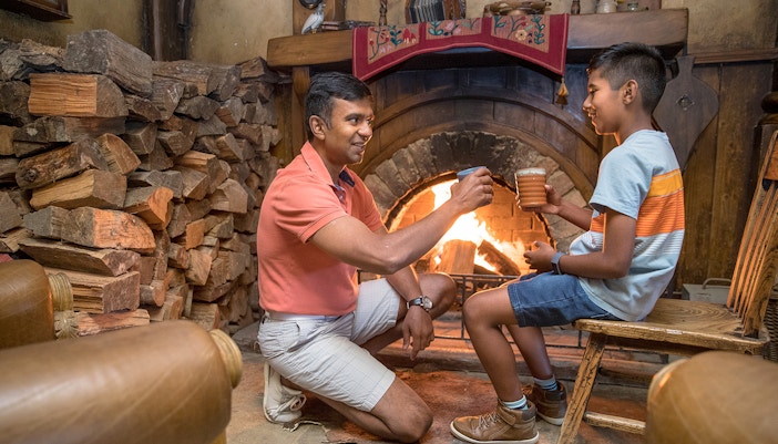 Father and son enjoying drinks by the fireplace at Hobbiton Movie Set, New Zealand.