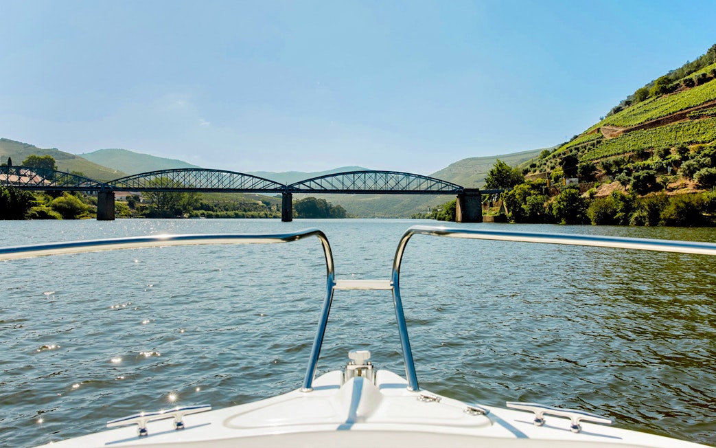 Boat view of bridge and vineyards on Douro River in evening.