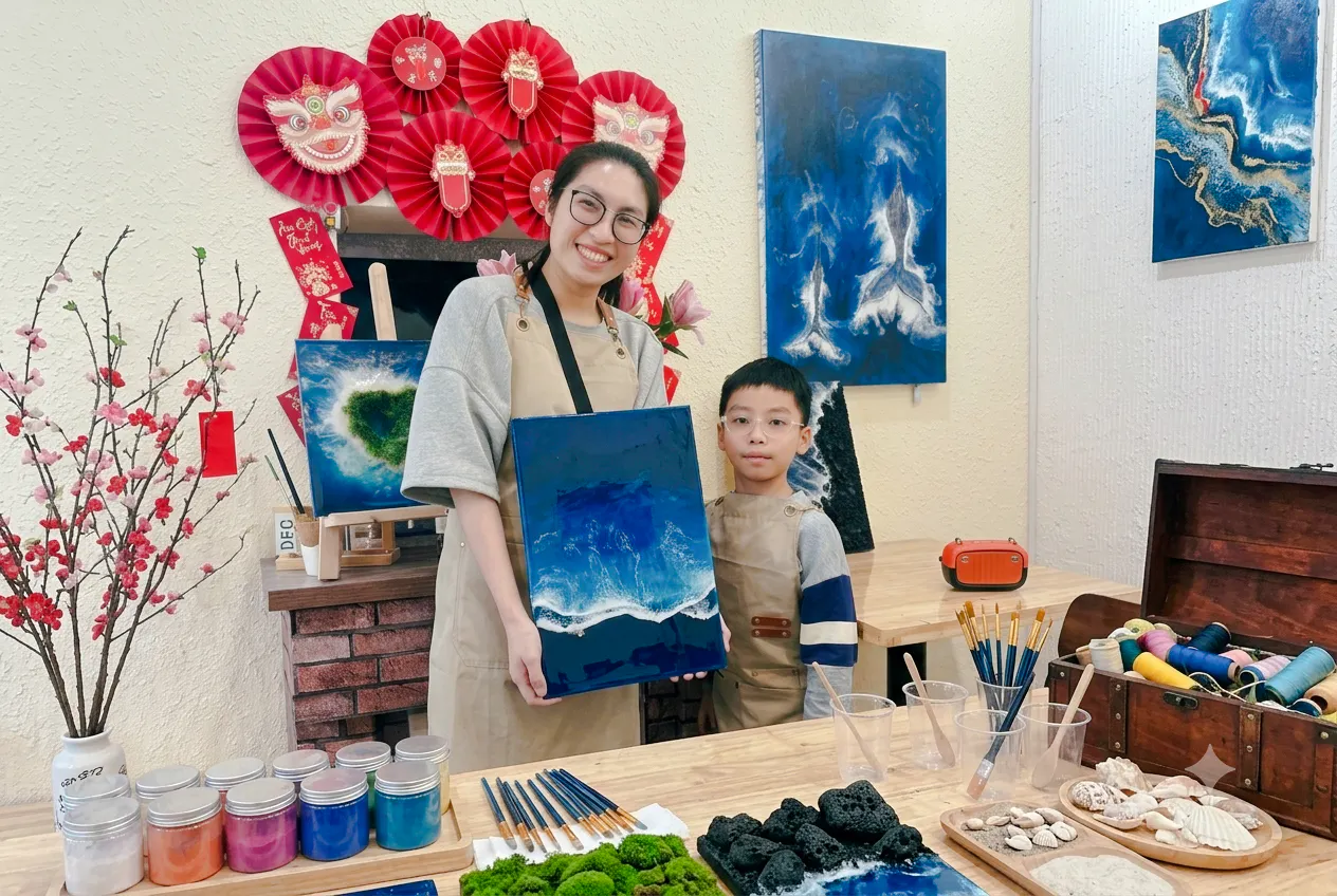 Creating artwork in a Hanoi studio with a woman and child displaying a blue ocean painting.