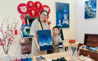 Creating artwork in a Hanoi studio with a woman and child displaying a blue ocean painting.