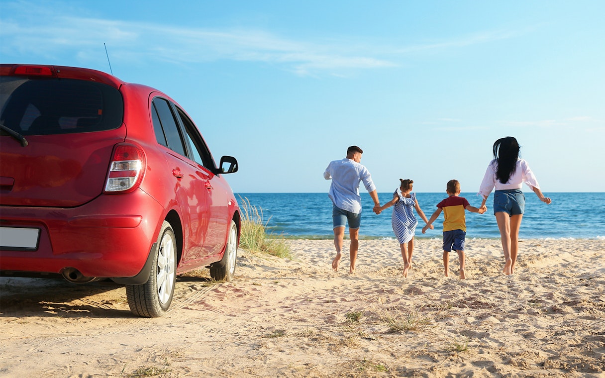 Family walking on Langkawi beach near parked car.