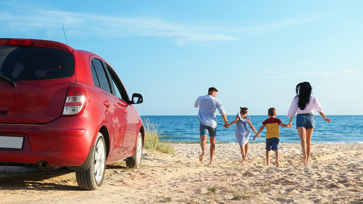 Family walking on Langkawi beach near parked car.
