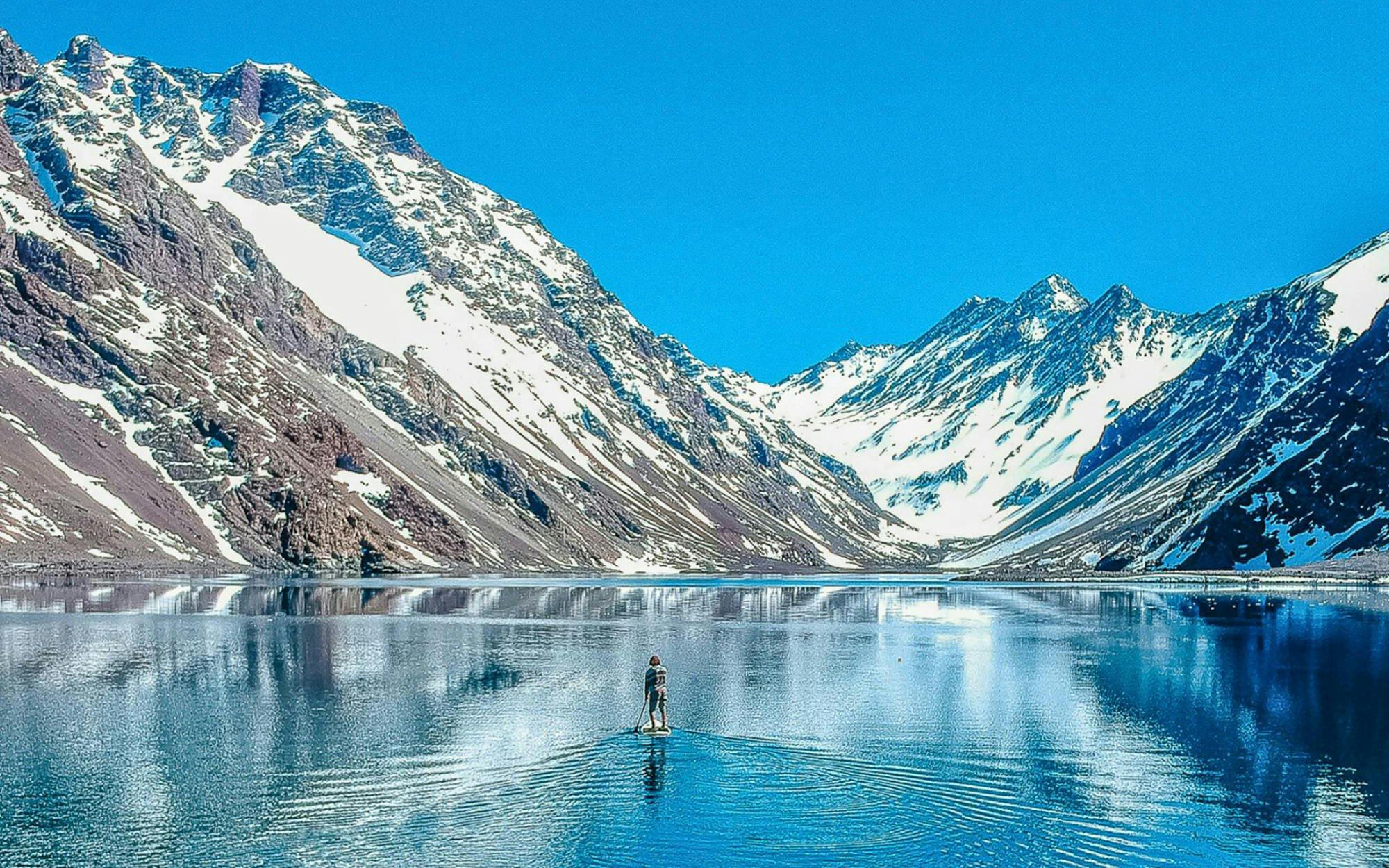Paddleboarder on Laguna del Inca with snow-capped Andes mountains in the background.