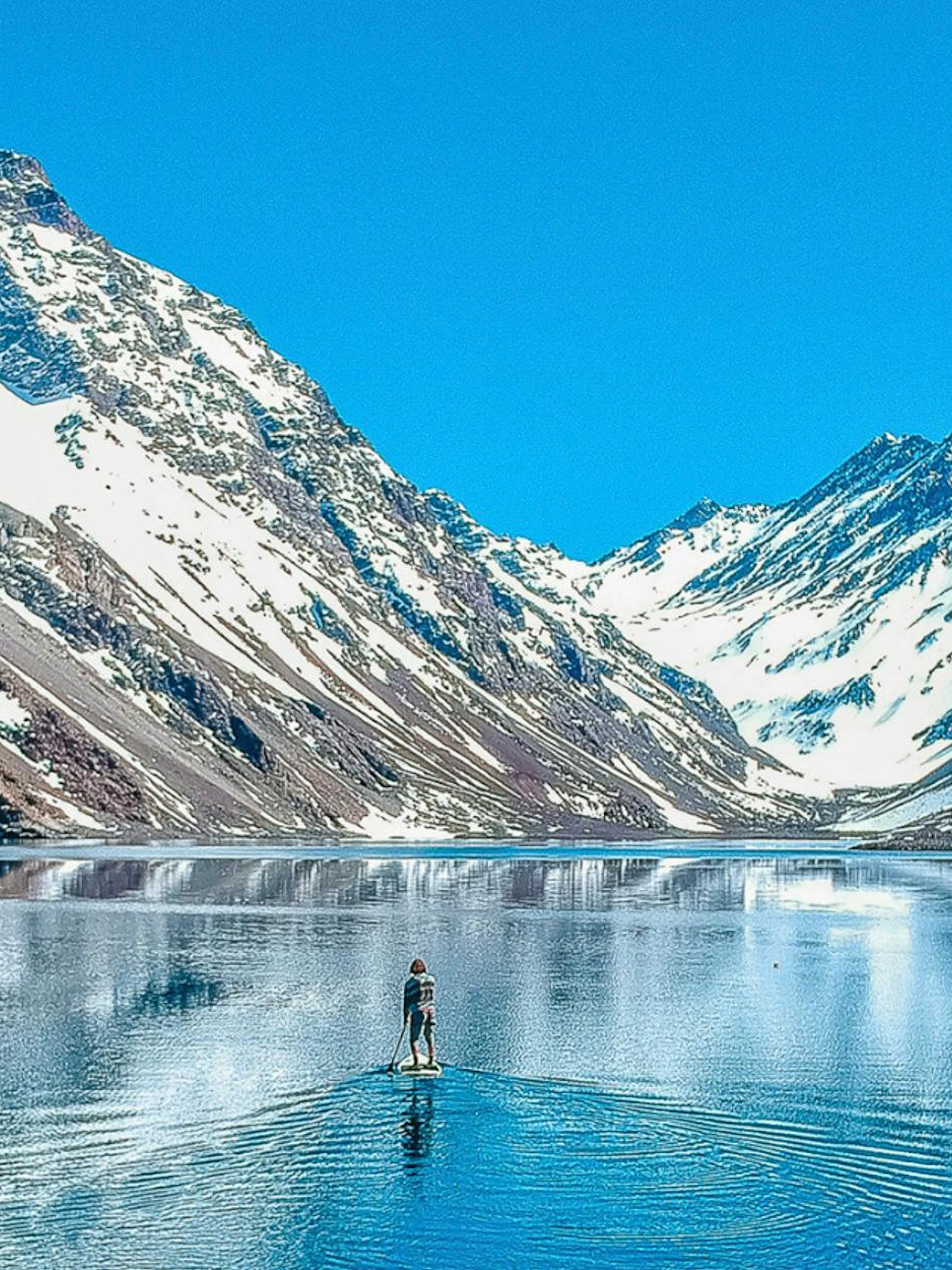 Paddleboarder on Laguna del Inca with snow-capped Andes mountains in the background.