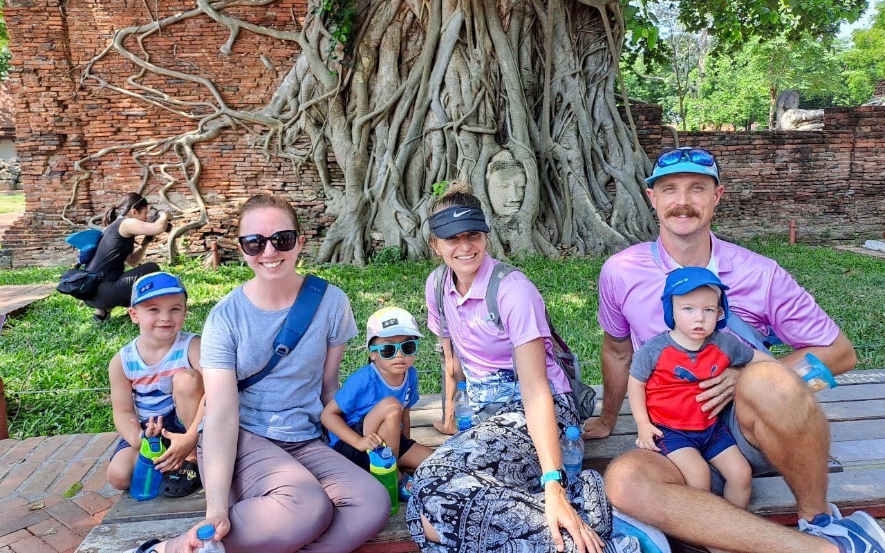 Family posing near Buddha head entwined in tree roots, Ayutthaya City bicycle tour.