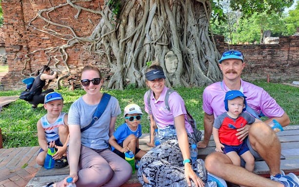 Family posing near Buddha head entwined in tree roots, Ayutthaya City bicycle tour.