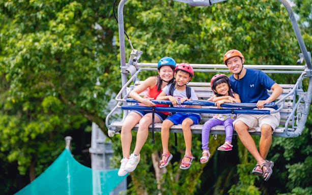 Family enjoying Skyline Luge Singapore ride with lush greenery in the background.
