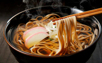 Steaming bowl of Japanese soba noodles with chopsticks and fish cake slices.