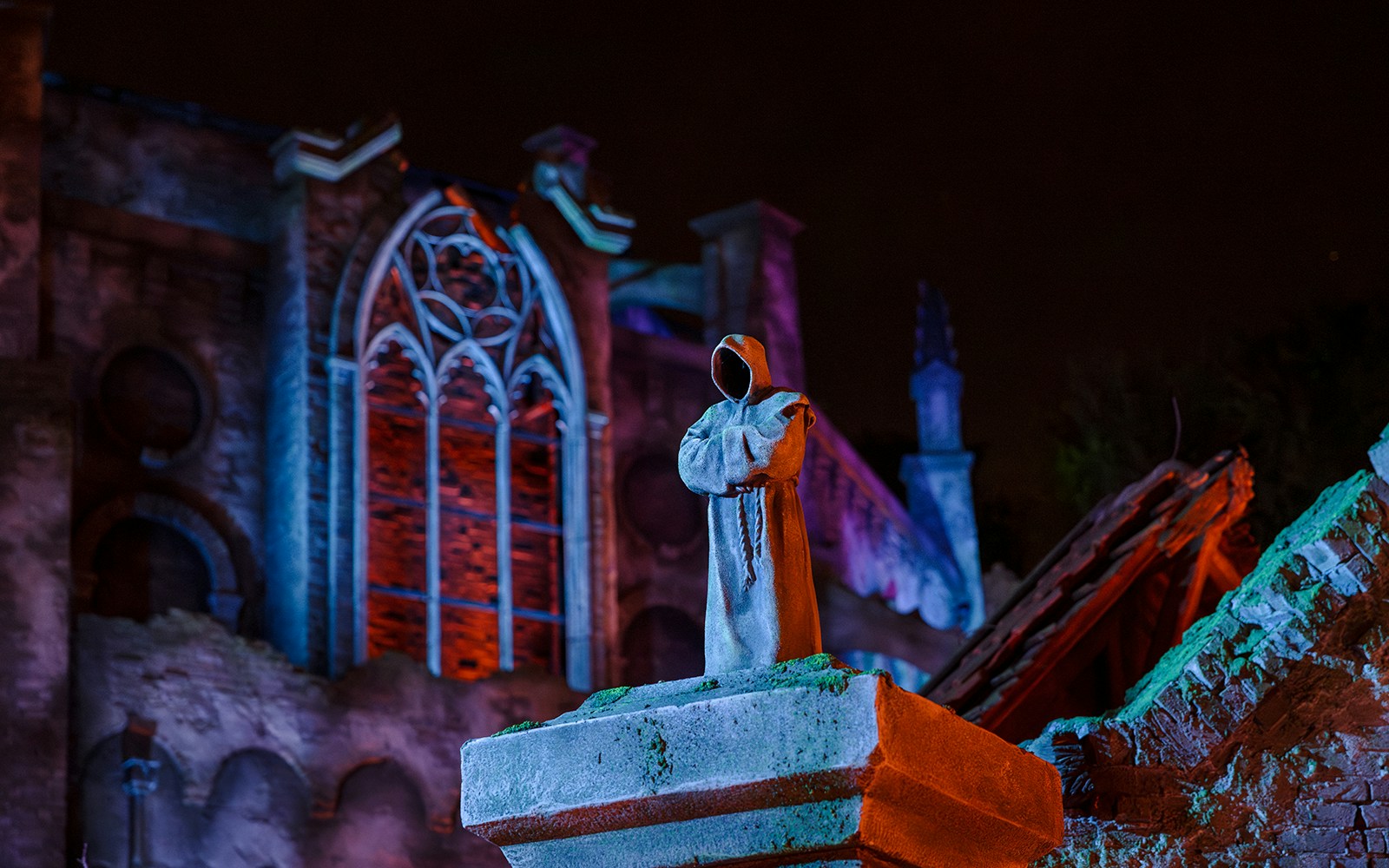 Hooded statue in front of illuminated gothic architecture at Efteling Theme Park.