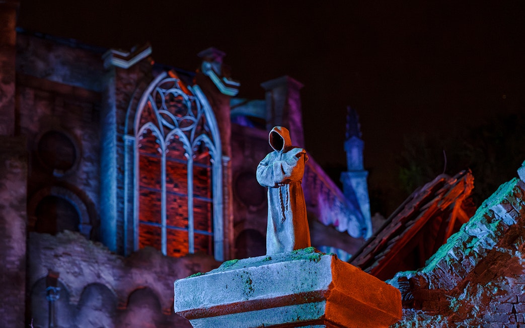 Hooded statue in front of illuminated gothic architecture at Efteling Theme Park.