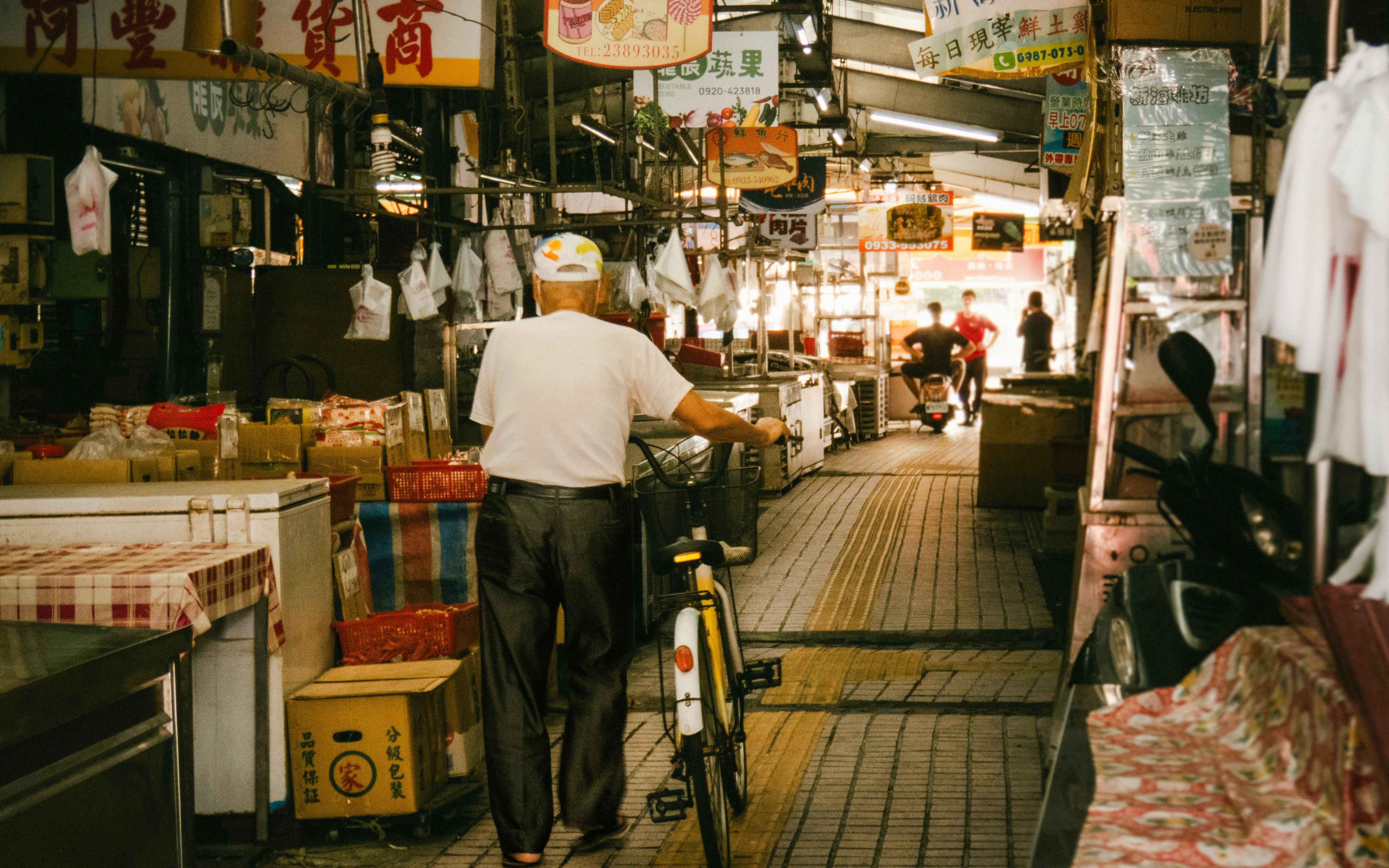 Man with bicycle in a bustling Tokyo market, surrounded by colorful signs and stalls.