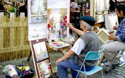 Artist painting street scene in Montmartre, Paris with Eiffel Tower artwork displayed.