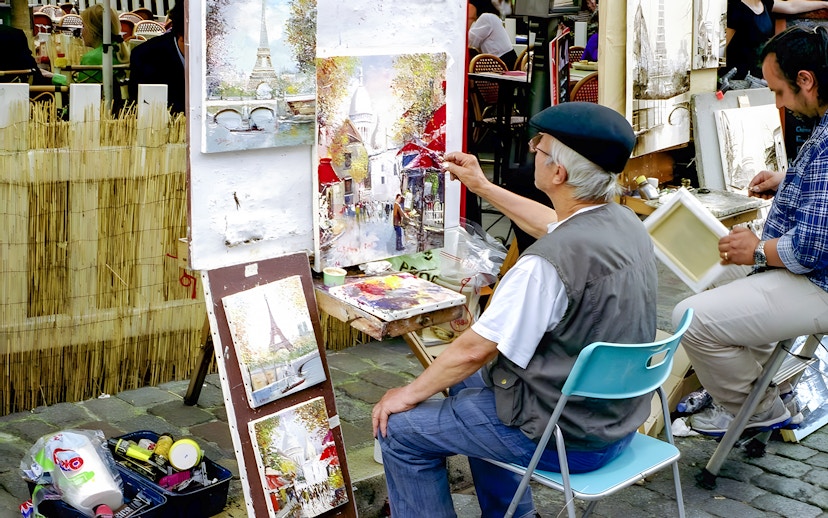 Artist painting street scene in Montmartre, Paris with Eiffel Tower artwork displayed.