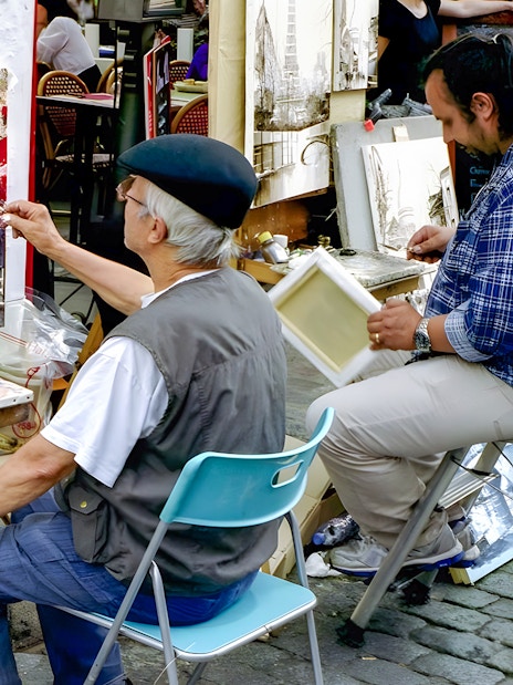 Artist painting street scene in Montmartre, Paris with Eiffel Tower artwork displayed.