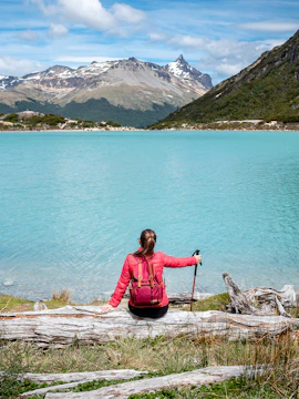Woman sitting by Emerald Lagoon in Ushuaia, Argentine Patagonia, with mountain views.