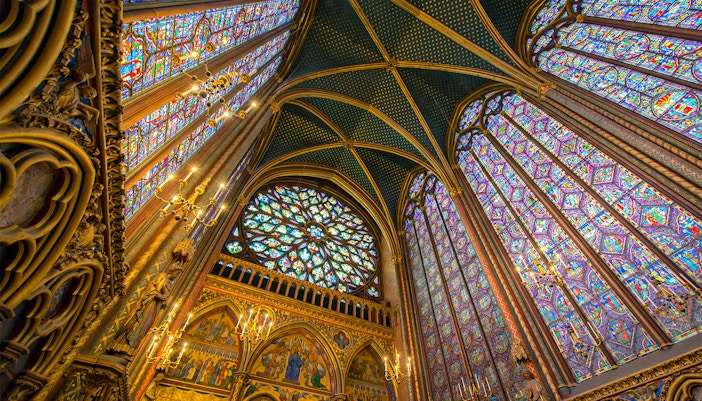 Rose window with golden columns and motifs, viewed from below in a historic cathedral.