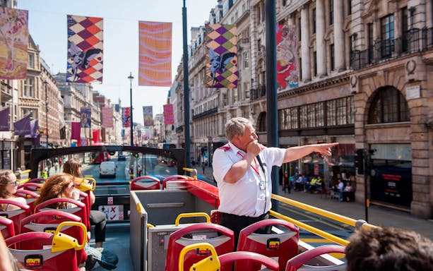Tour guide speaking on a Tootbus in London, with passengers enjoying city views.