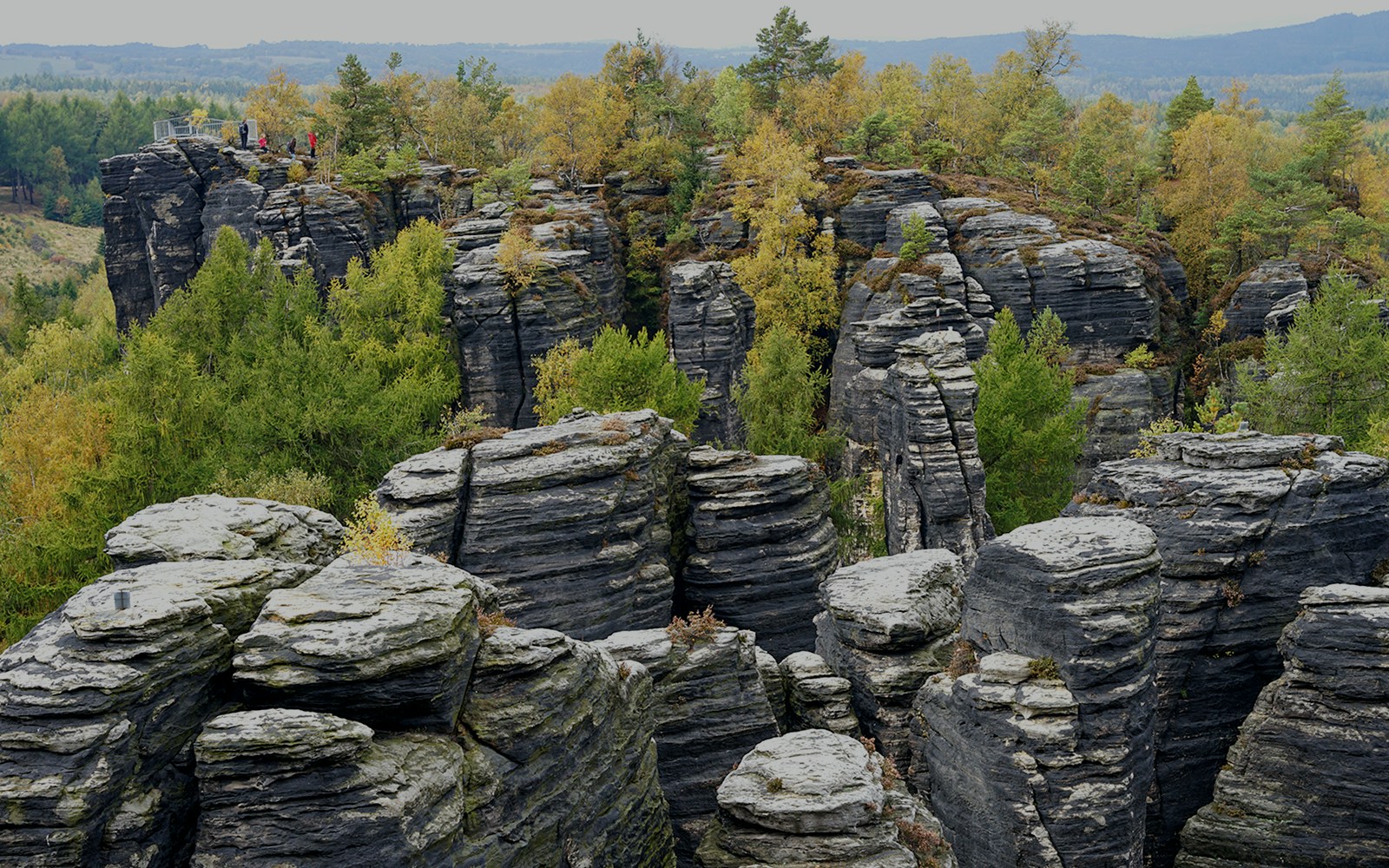 Sandstone rock formations at Tisa Walls Labyrinth with trees and distant hills.